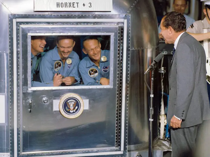 President Nixon welcomes Armstrong, Collins and Aldrin, sealed in the Mobile Quarantine Facility aboard USS Hornet, 24 July 1969