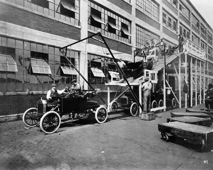 Car bodies slide down a ramp onto finished chassis outside the Highland Park plant, 1913.