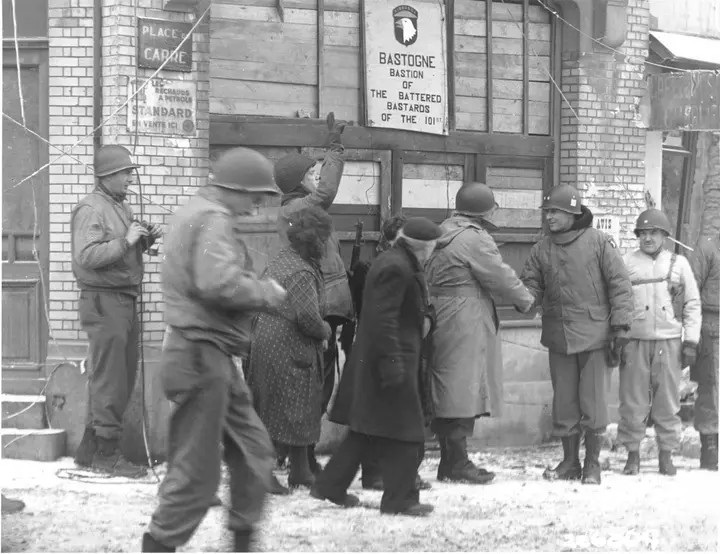 Generals of the 101st review the division in Bastogne beneath the sign its men put up: Bastion of the Battered Bastards of the 101st, January 1945