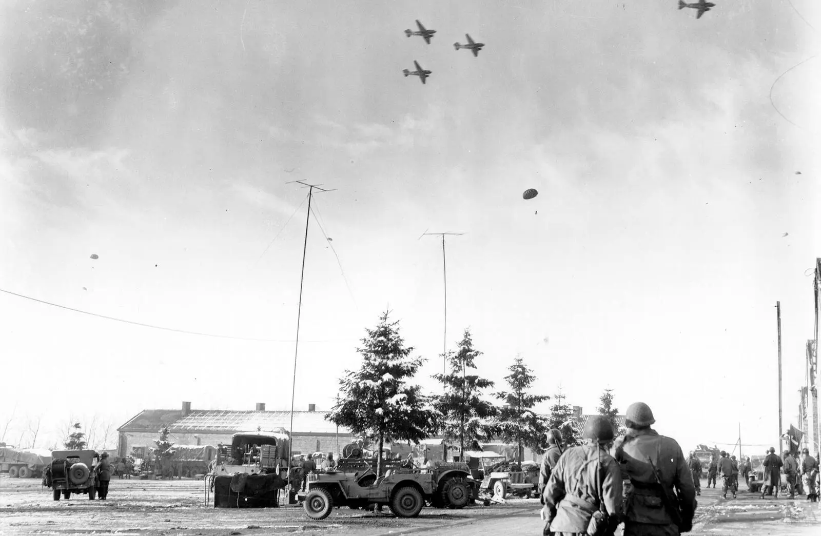 Men in Bastogne look up as C-47s drop supplies to the surrounded garrison, 26 December 1944
