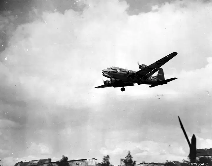 A C-54 Skymaster makes a Little Vittles candy drop on approach to Berlin. The tiny parachutes are visible below its tail.