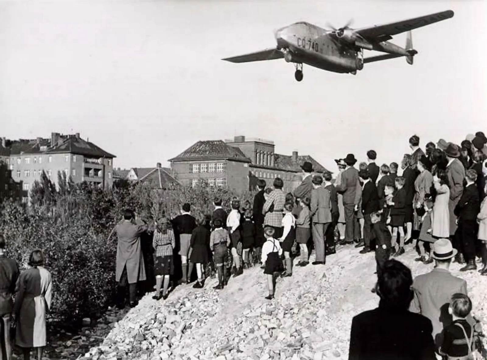 Berliners on a mound of rubble watch an American C-82 Packet come in low over the city, 1948.