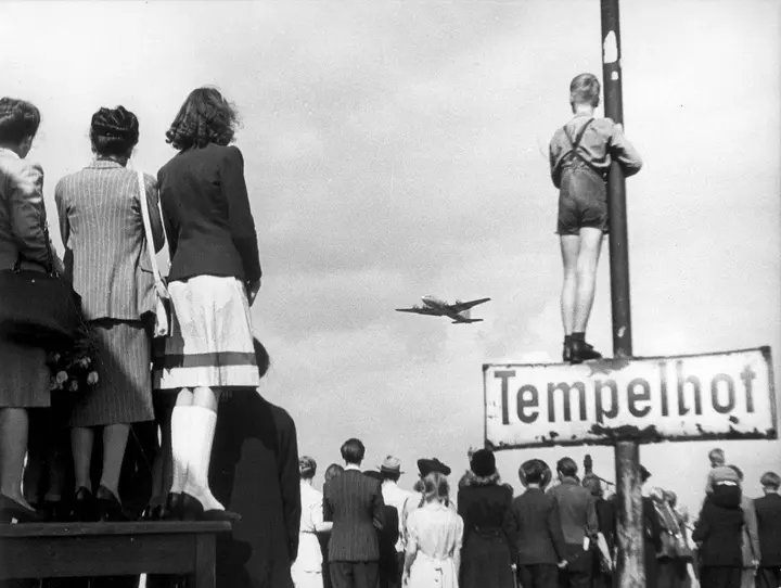 Berliners line the edge of Tempelhof to watch an airlift transport land, 1948.
