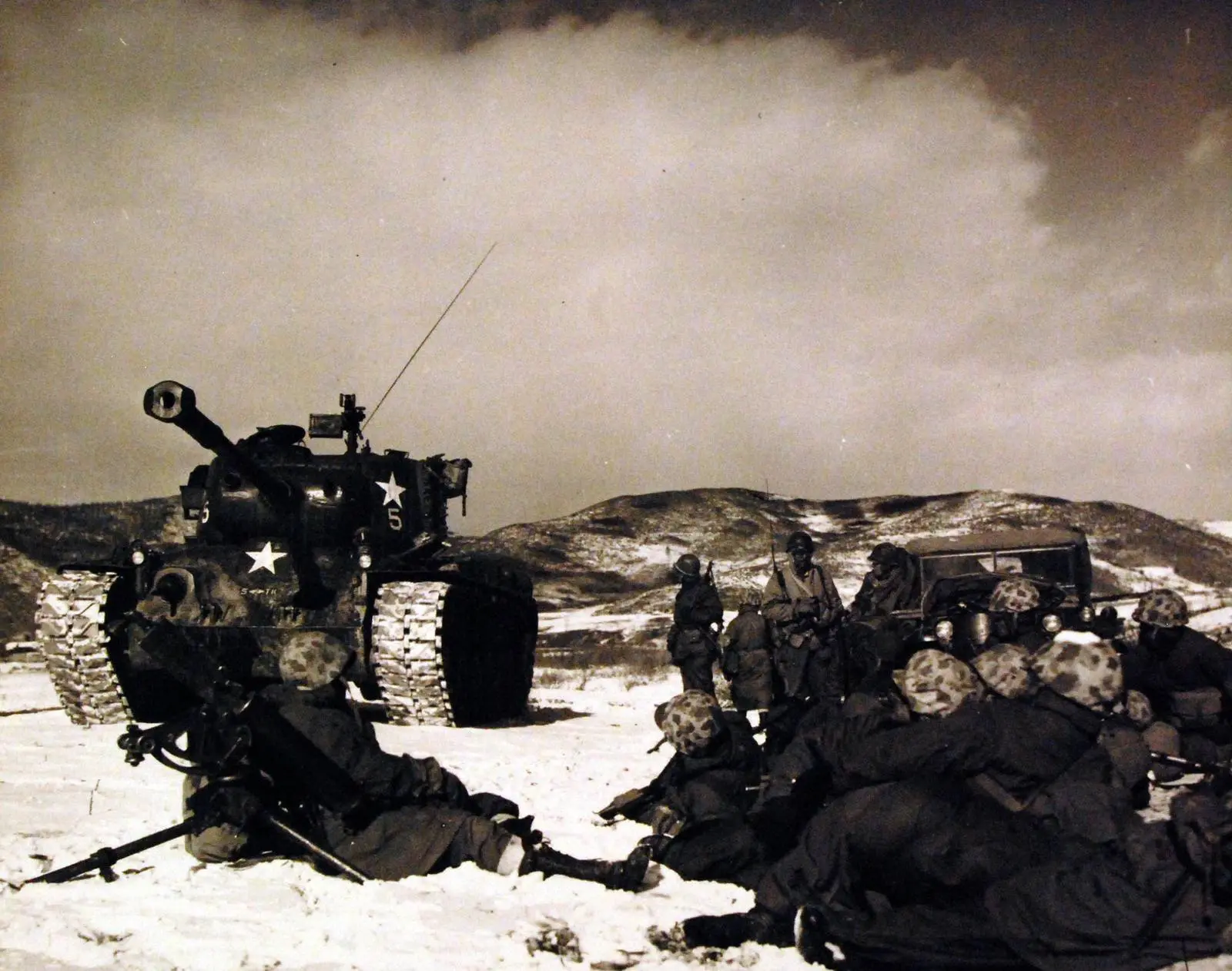 1st Marine Division Marines rest beside a tank on a snow-covered roadside after beating off an ambush, December 1950 (A-5469)