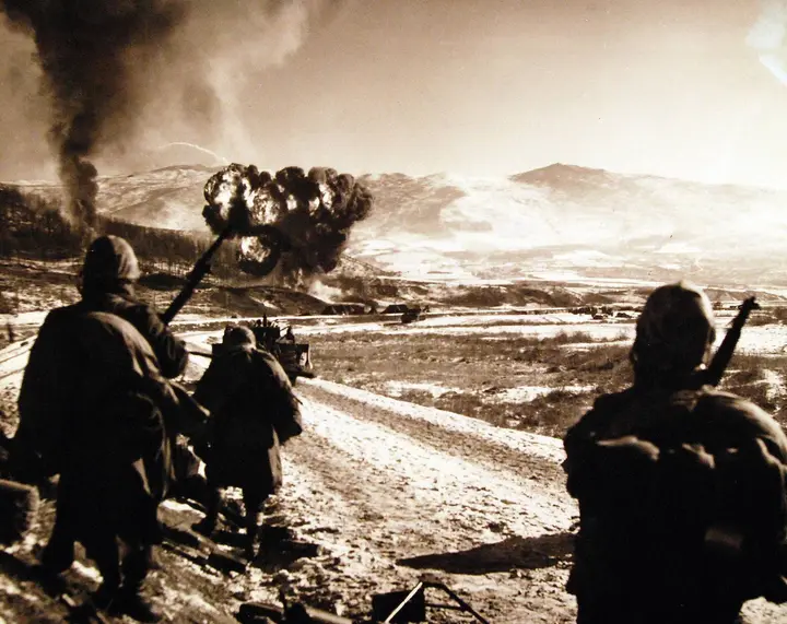 A Marine Corsair pulls up through the smoke after a napalm strike as 7th Marines watch from the road south of Hagaru-ri, 6 December 1950 (A-5464)