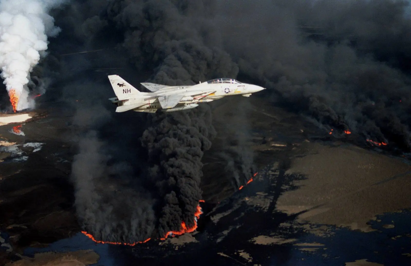 A Navy F-14A Tomcat of Fighter Squadron 114 flies over a Kuwaiti oil well set ablaze by Iraqi troops, 1991.