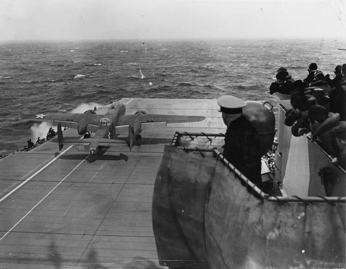 A B-25 starts its takeoff run down Hornet’s wet flight deck on 18 April 1942 while officers watch from the bridge wing.