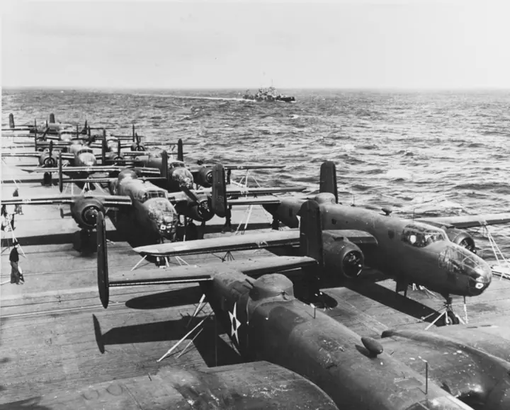 Eight of the sixteen B-25Bs lashed to Hornet’s flight deck on the way to the launch point, with the cruiser Nashville in the distance (NH 53421).