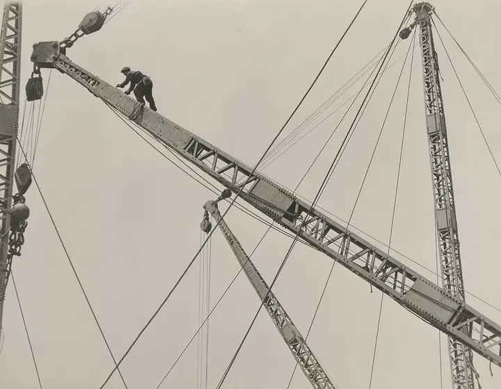 Jumping the derrick: an ironworker walks the boom of a derrick high over the city.
