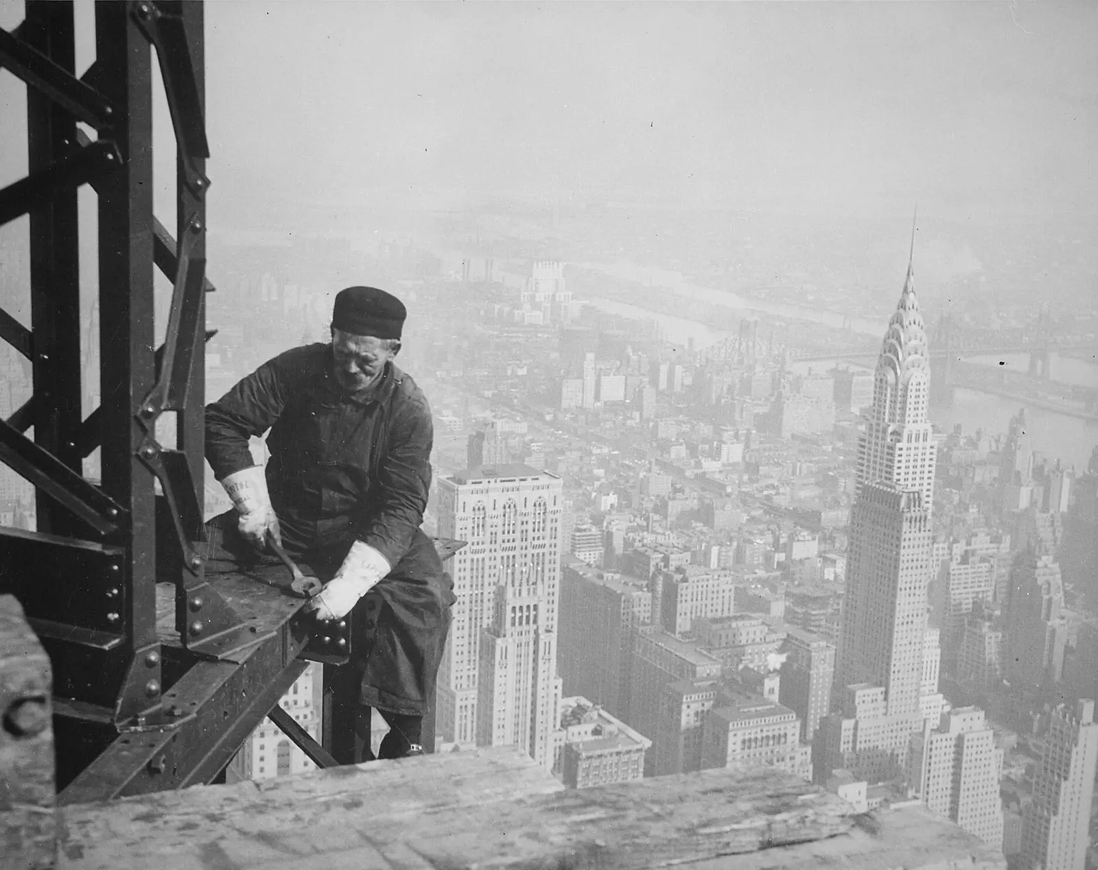 A structural worker bolts a beam high on the Empire State Building, with the Chrysler Building behind him.