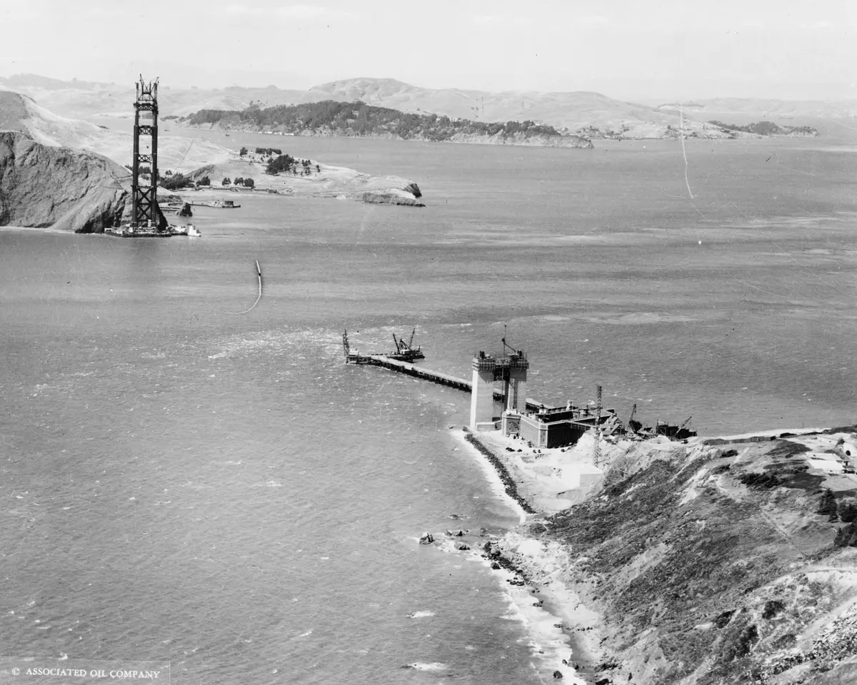 The work trestle reaches out from Fort Point toward the south pier site in the open strait, with the newly finished north tower beyond, 16 July 1934.