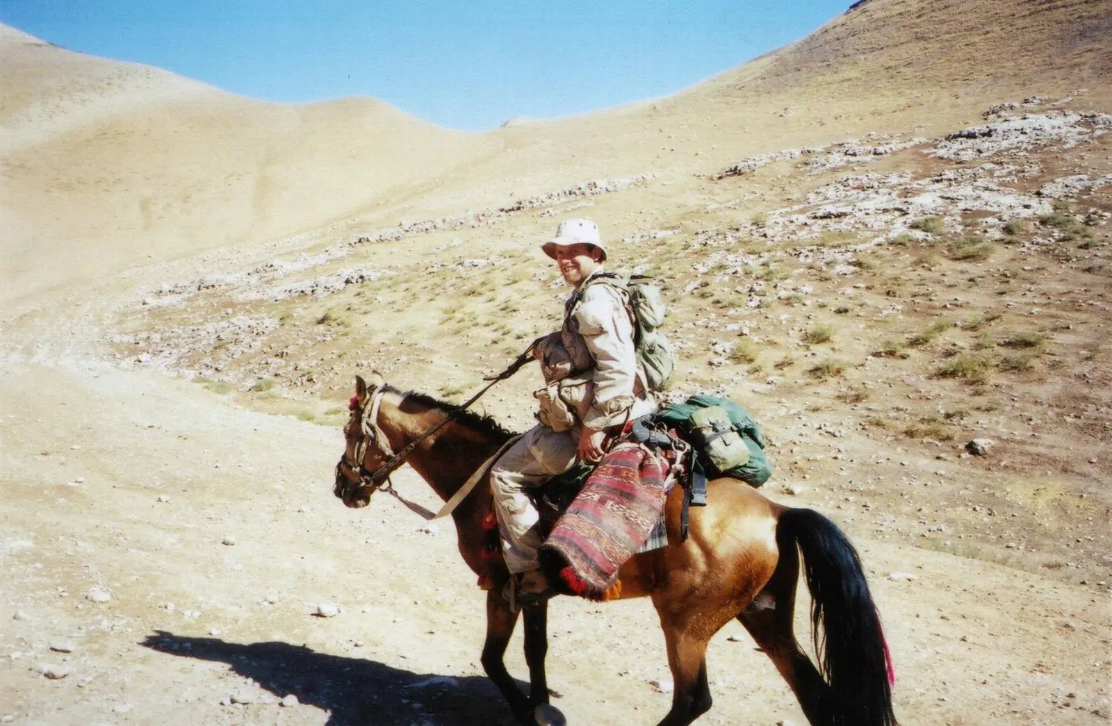 A Green Beret on a small Afghan horse, saddlebags of Afghan carpet behind him, in the hills of northern Afghanistan, 2001