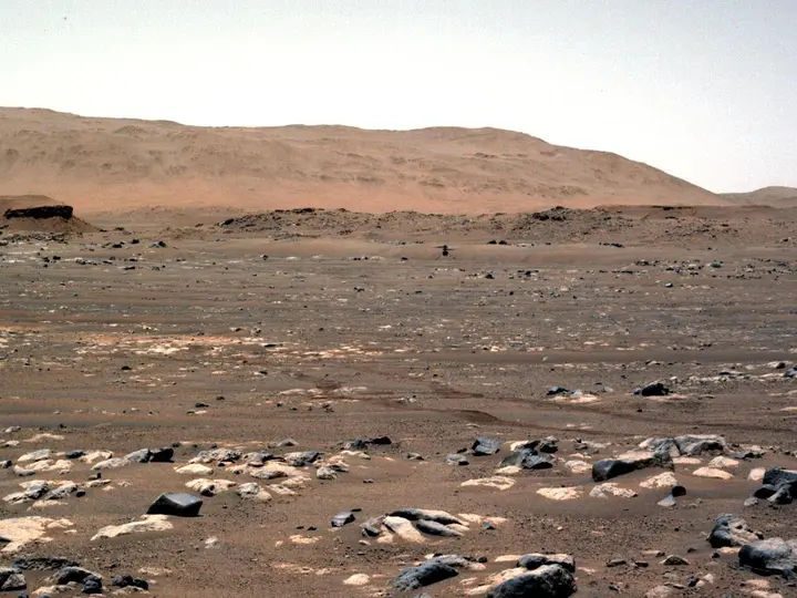 Ingenuity hovers over Wright Brothers Field on the first powered, controlled flight on another planet, seen by Perseverance's Navcam from 210 feet away, 19 April 2021