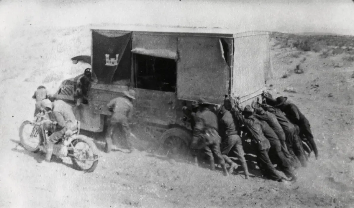 Soldiers of the 1919 Army transcontinental convoy put their shoulders to an engineer truck stuck in desert sand.