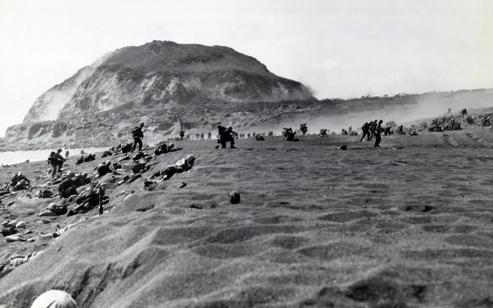 Marines charge inland across the volcanic sand at the foot of Mount Suribachi, 19 February 1945
