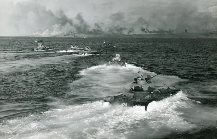 A wave of Marine amphibian tractors churns toward the smoke-shrouded beaches as a cruiser shells Suribachi, 19 February 1945