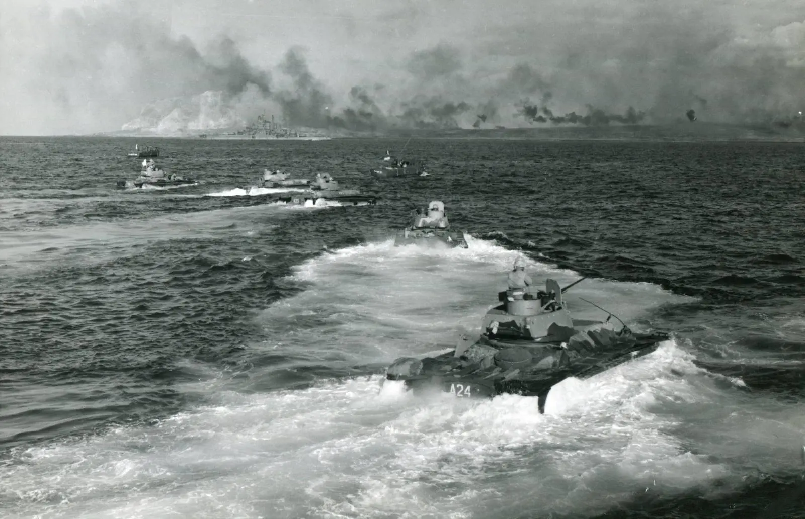 A wave of Marine amphibian tractors churns toward the smoke-shrouded beaches as a cruiser shells Suribachi, 19 February 1945
