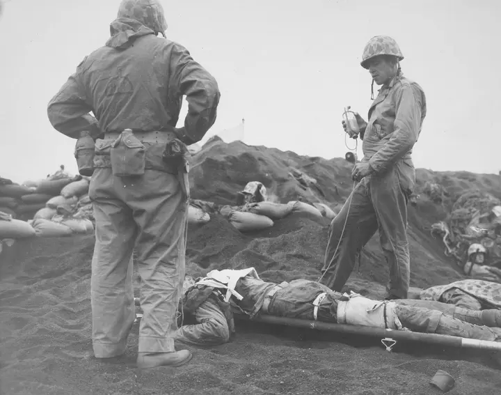Navy corpsman Arthur H. Clayton gives a blood transfusion to a wounded Marine on the beach, February 1945