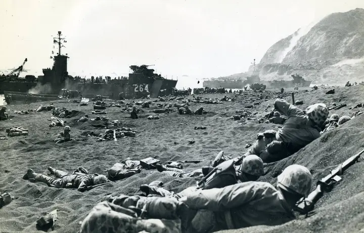 4th Marine Division Marines dig into the black sand as landing ships unload under Mount Suribachi, 19 February 1945