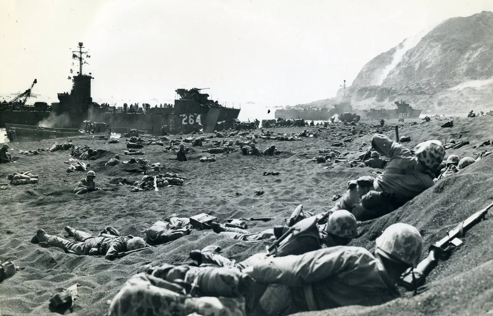 4th Marine Division Marines dig into the black sand as landing ships unload under Mount Suribachi, 19 February 1945