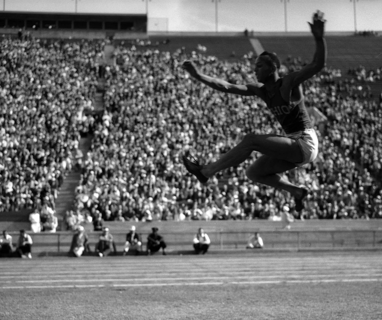 Owens in mid-flight over the long jump pit before a packed stadium in California in the 1930s