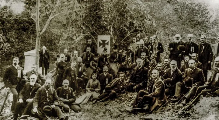 Veterans of the 20th Maine gather on Little Round Top in 1889, with Chamberlain seated at center right between the Fifth Corps cross and the regimental flag.