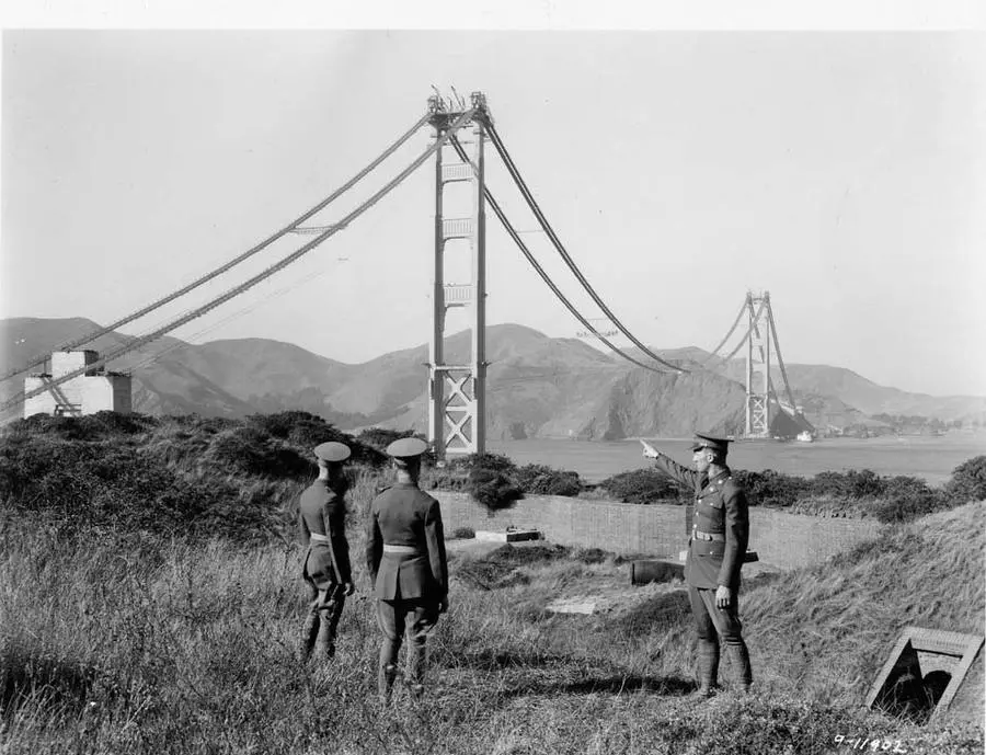 Army officers at Fort Scott look out at the unfinished bridge, its catwalks strung between the towers, mid-1930s.