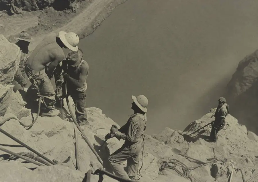 Shirtless high scalers drill the canyon wall high above the Colorado River, photographed by Ben Glaha, c. 1934