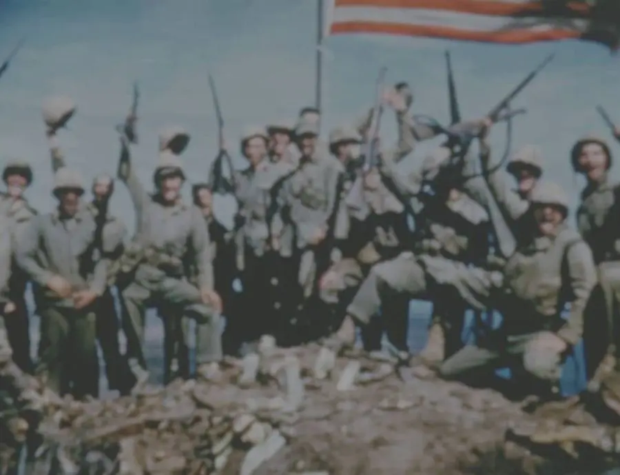 Marines cheer beneath the second flag on Mount Suribachi in Sgt. Bill Genaust's color film, 23 February 1945