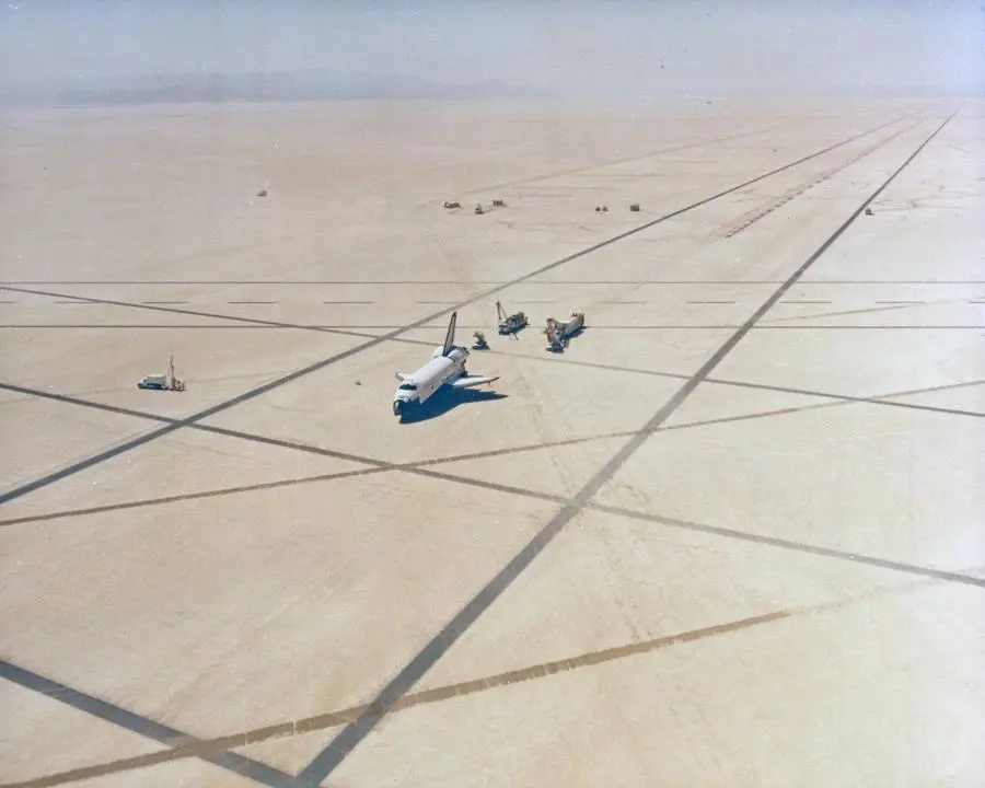 Columbia on Runway 23 of Rogers Dry Lake after landing, seen from the air as the convoy tows it to its parking area, 14 April 1981 (KSC-81PC-0426)