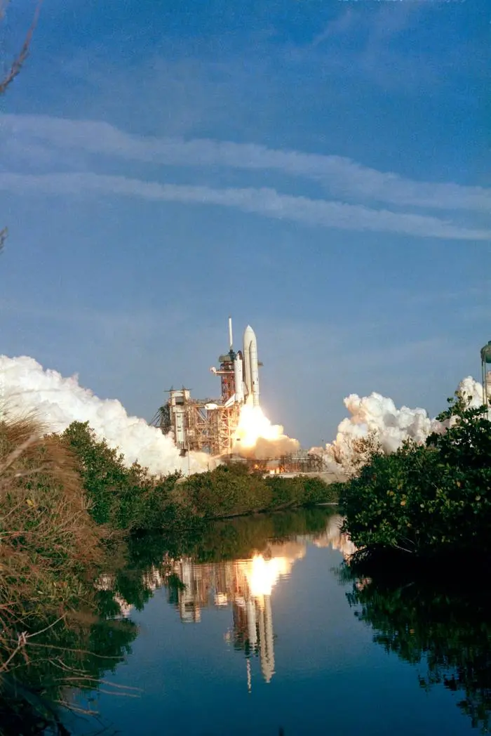 Columbia rises off Pad 39A, reflected in the water near the launch complex, 12 April 1981 (S81-30462)