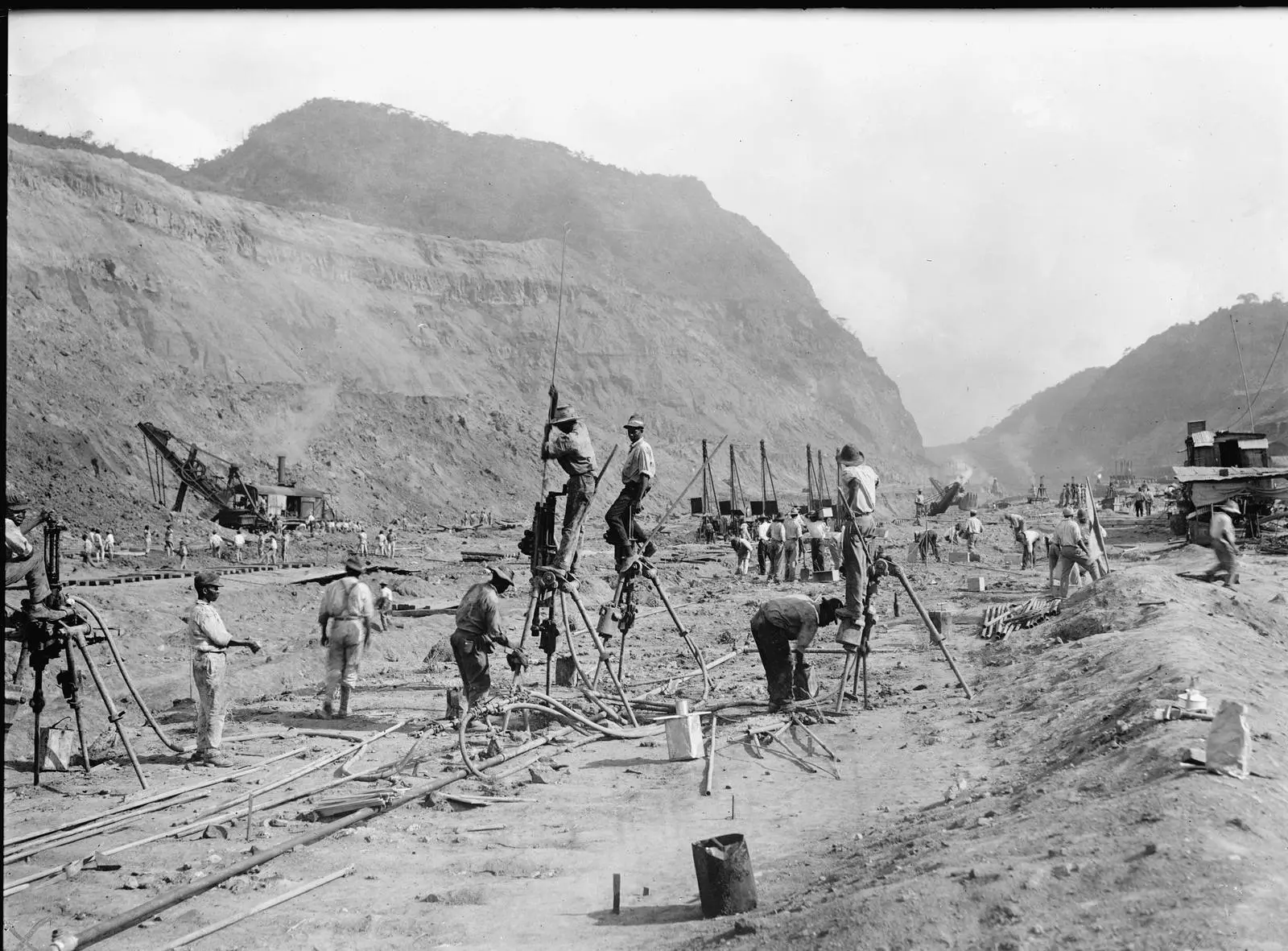 Drill crews at work on the floor of the Culebra Cut, with steam shovels behind them and the walls of the Continental Divide rising above, 1913
