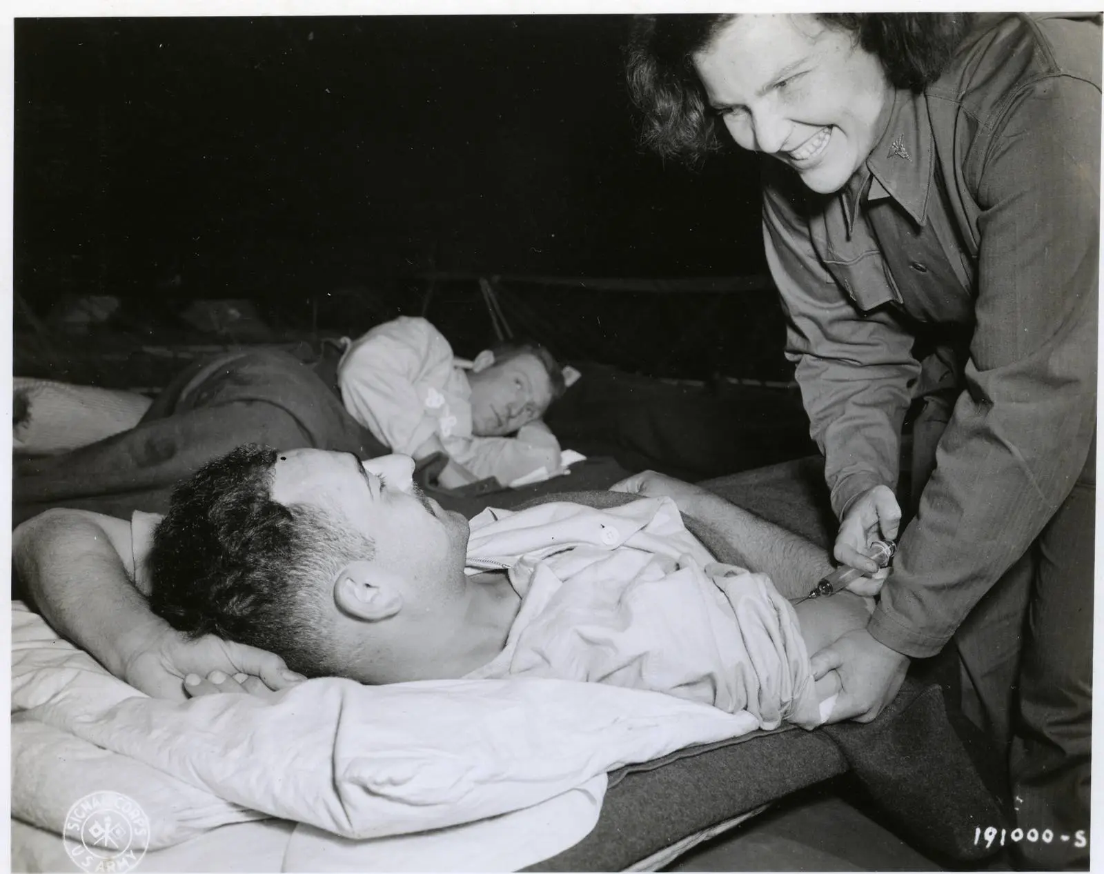 Army nurse Lt. Gertrude A. Nolan gives an injection to Sgt. Charles A. Comar of New York City in an evacuation hospital in Normandy, 5 July 1944.