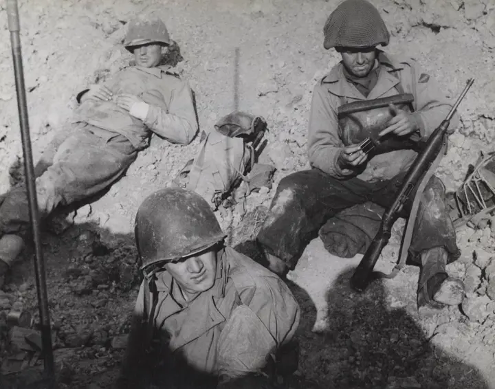Rangers take a breather in a foxhole on Pointe du Hoc in June 1944, weapons close at hand.