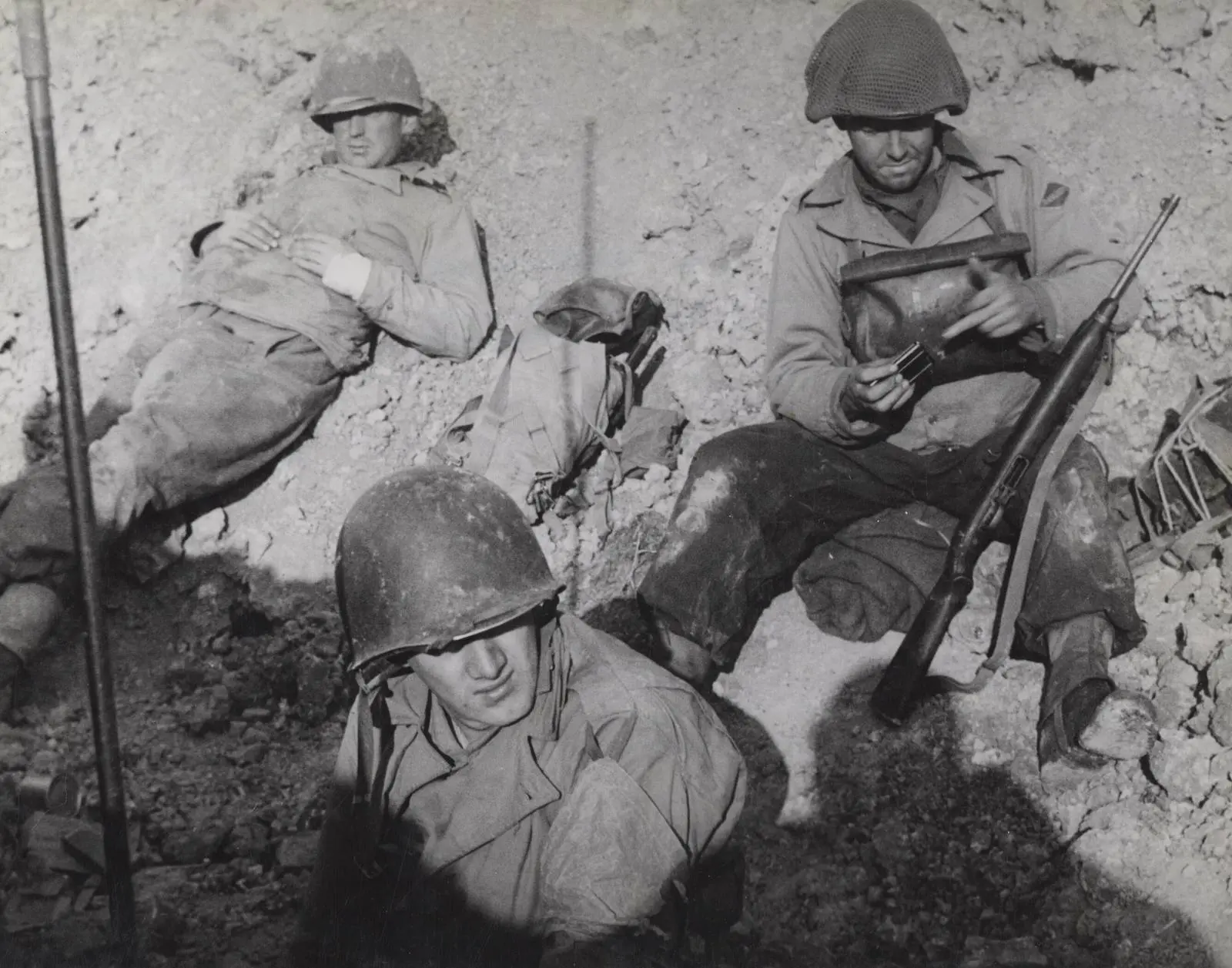Rangers take a breather in a foxhole on Pointe du Hoc in June 1944, weapons close at hand.