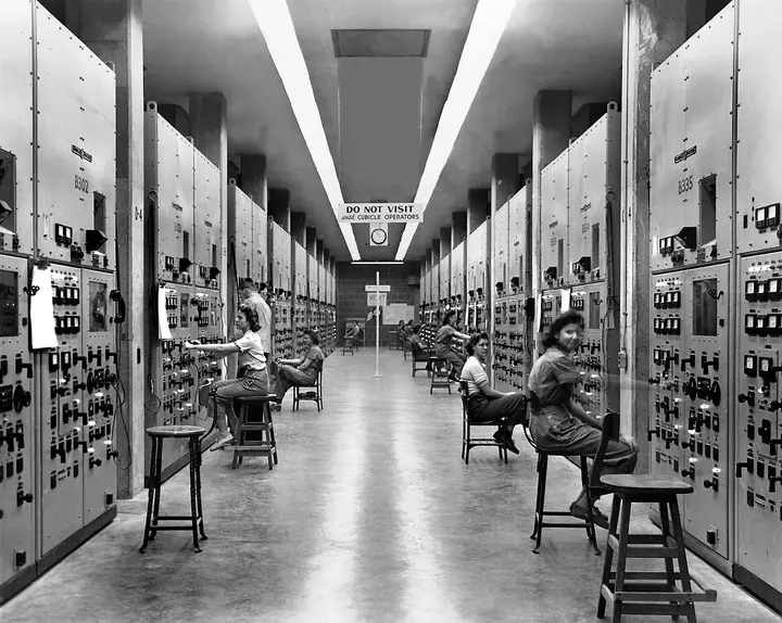 Calutron operators at their control panels in the Y-12 plant at Oak Ridge, 1944, under a sign reading Do Not Visit with Cubicle Operators.