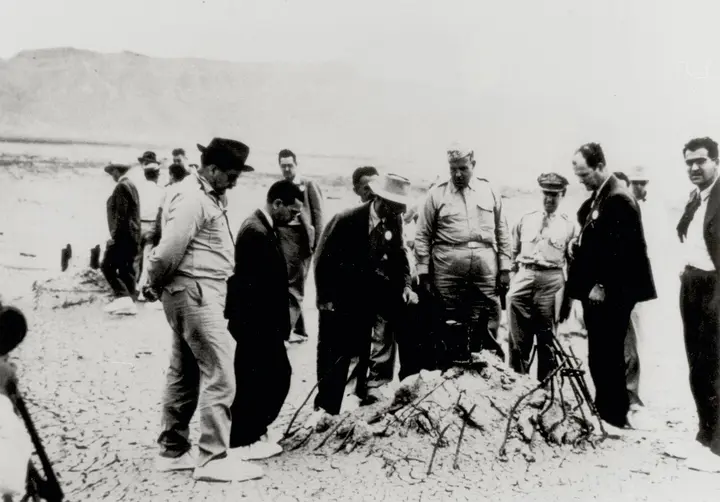 Oppenheimer (light hat) and Groves (in uniform) at the rubble of the Trinity tower at ground zero, September 1945.