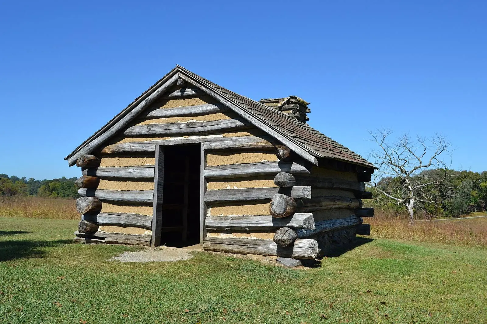 A reconstructed soldiers’ hut at Valley Forge: log walls chinked with clay, a slab roof and the door in the end.