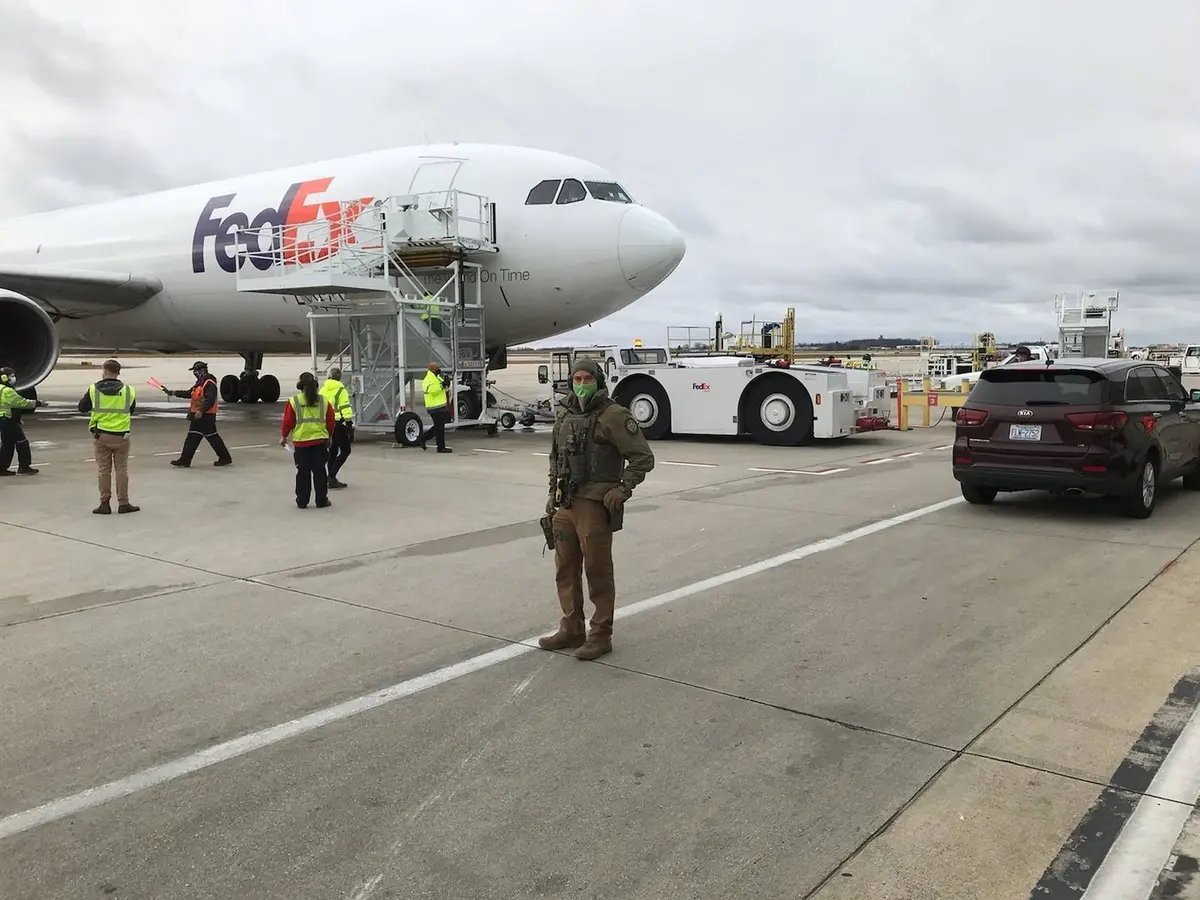 A Deputy U.S. Marshal stands guard on the tarmac as the first COVID-19 vaccine shipments move by FedEx, 14 December 2020.